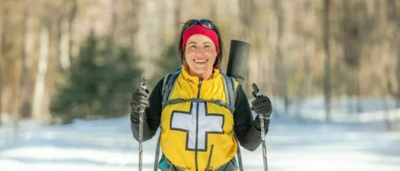 Volunteer wearing a first aid vest, on a ski trail, approaching the camera.