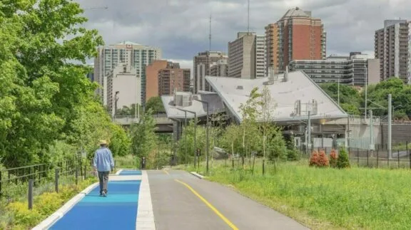 Separate bicycle path and footpath. People walking on the footpath; the O-Train's Pimisi station is in the background.