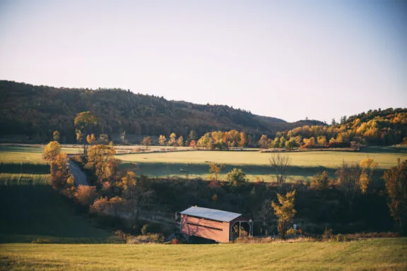 An open pastoral landscape featuring a covered bridge, in the fall.