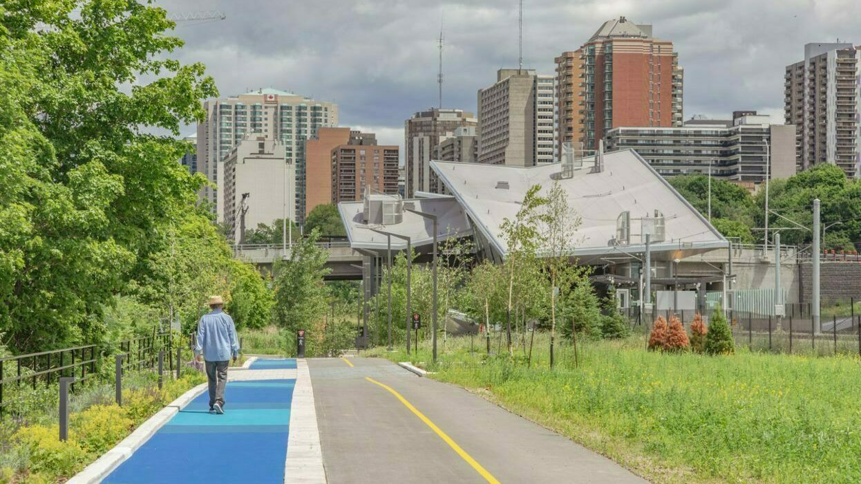 Separated cycling lane and pedestrian pathway with a person walking toward the Pimisi O-Train station.