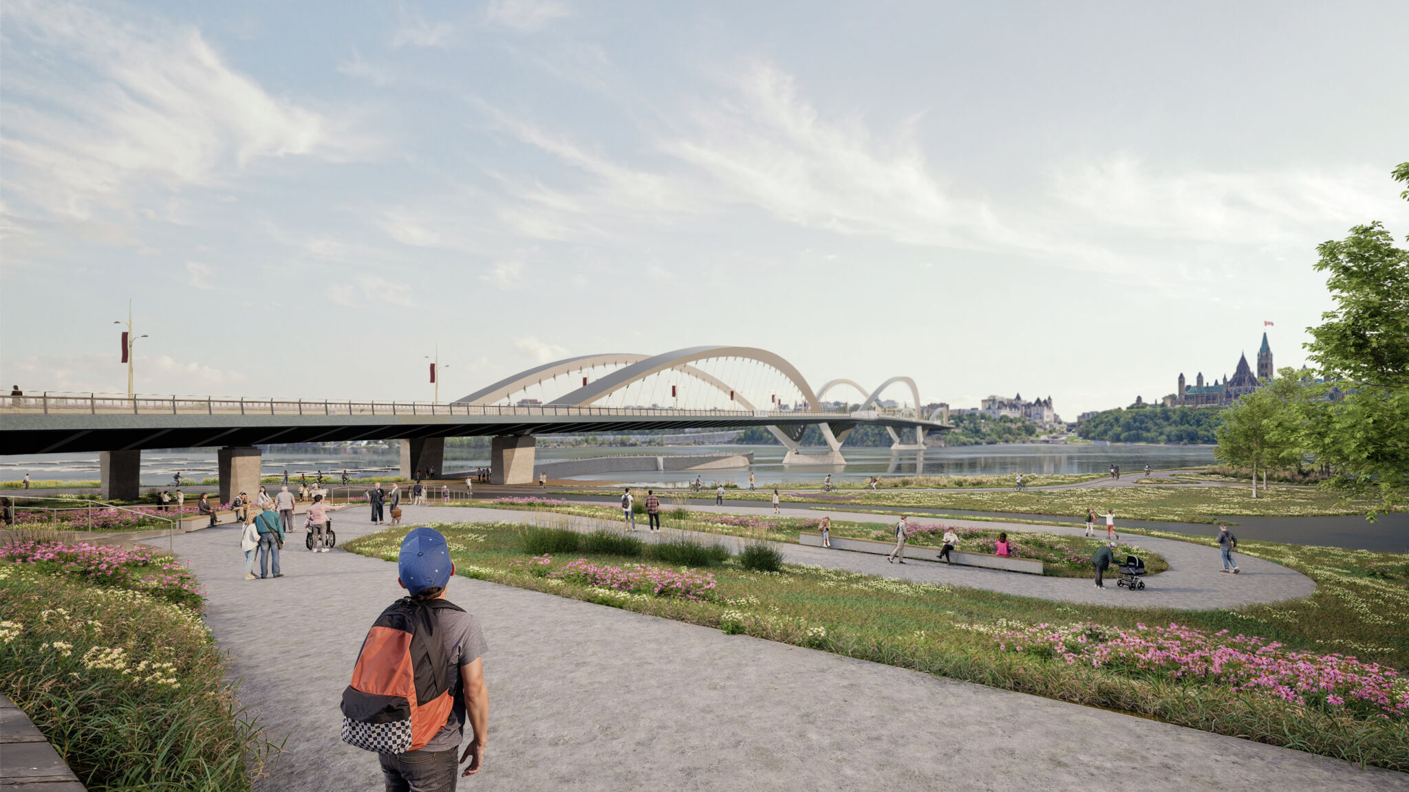 View of the riverbank in Gatineau and the bridge spanning the river. A pathway connects the bridge to the multi-use pathways. People are walking, cycling and enjoying the pathways along the shore. The area is landscaped with greenery and flowers. Buildings and structures are visible across the water.