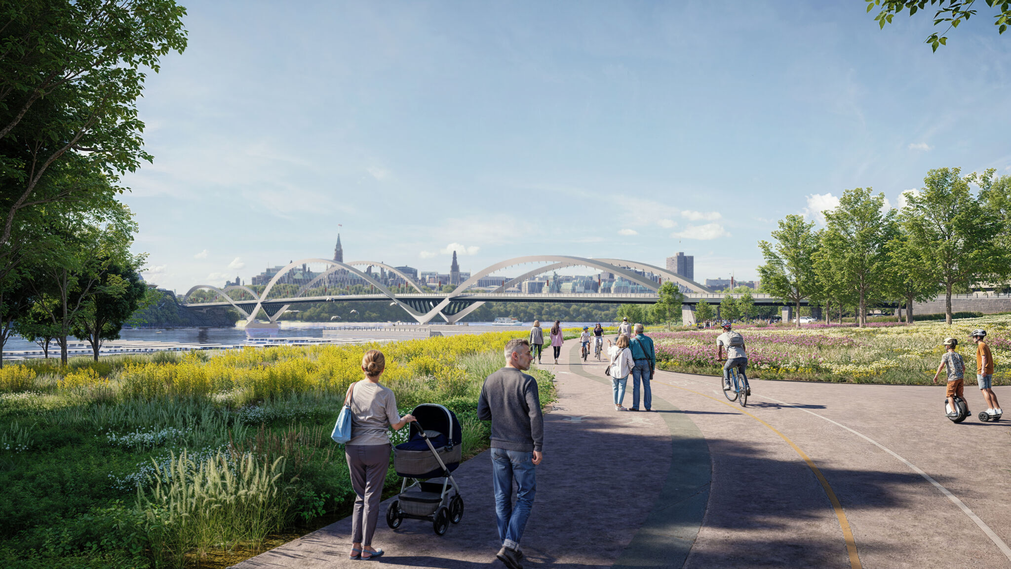 View of the riverbank and bridge from Jacques Cartier Park. The foreground features a paved pathway where people are walking, biking and using scooters. There is greenery and flowering plants on both sides of the path, and trees lining the area. The city skyline is visible in the distance beyond the bridge.