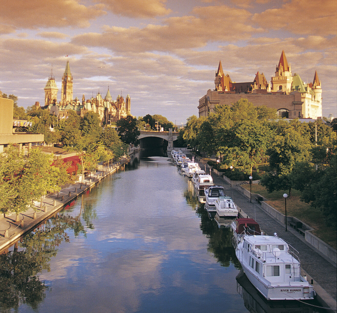 View of the Rideau Canal on a sunny evening with the Parliament and Fairmont Chateau Laurier in the background.